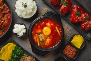 Sundubu Jjigae, sup tahu pedas khas Korea dengan telur mentah di atasnya, disajikan bersama nasi, kimchi, acar lobak, dan ayam goreng pedas