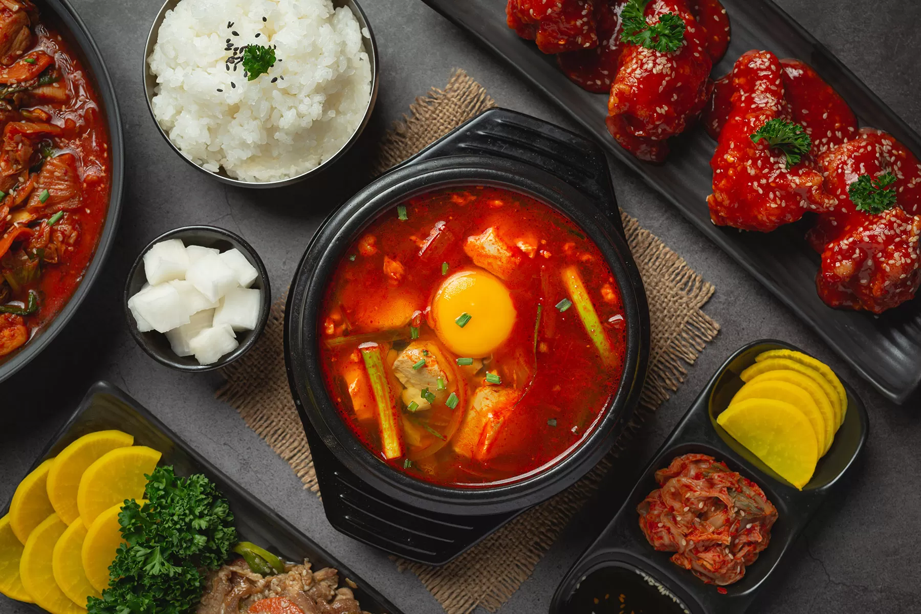 Sundubu Jjigae, sup tahu pedas khas Korea dengan telur mentah di atasnya, disajikan bersama nasi, kimchi, acar lobak, dan ayam goreng pedas