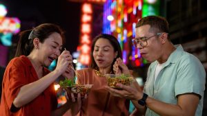 Tiga wisatawan mencicipi makanan lokal saat menjelajahi tempat makan di luar negeri pada malam hari.