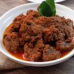 Rendang, hidangan khas Minangkabau yang terkenal di dunia, disajikan dalam piring putih dengan daun jeruk sebagai hiasan