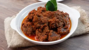 Rendang, hidangan khas Minangkabau yang terkenal di dunia, disajikan dalam piring putih dengan daun jeruk sebagai hiasan