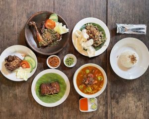 Aneka hidangan dari tempat makan hidden gem, dengan ayam goreng berbumbu, sup segar, dan lauk tradisional khas Indonesia, tersaji di atas meja kayu