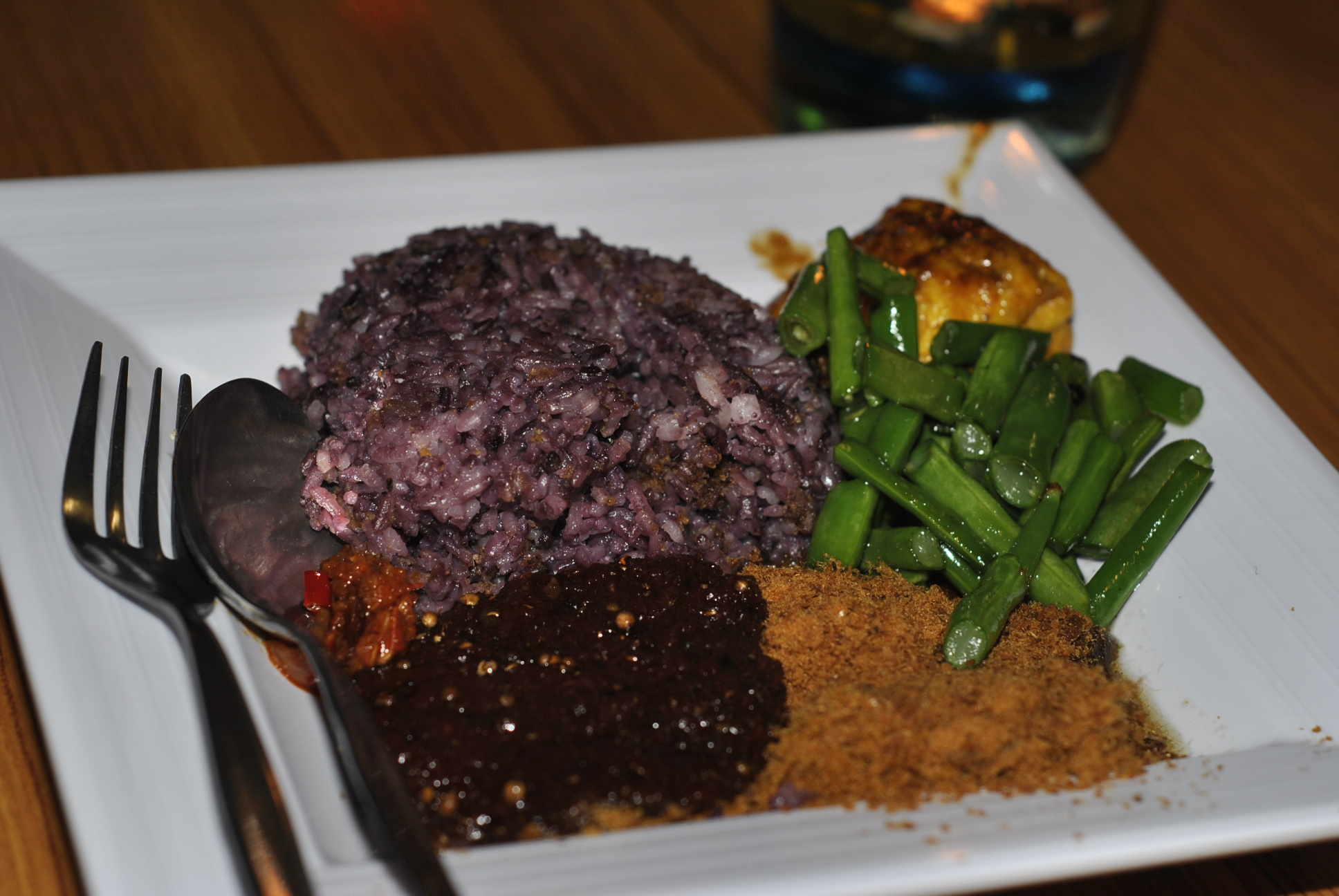 Makanan Hits yang Sering Dihype, Worth It atau Cuma Tren? Sepiring Nasi Kalong berwarna hitam keunguan, disajikan dengan lauk seperti tumis buncis, ayam, serundeng, sambal, dan saus hitam khas