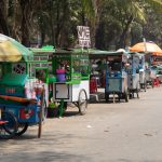 Gerobak makanan jalanan Indonesia dengan berbagai hidangan khas dan suasana ramai.