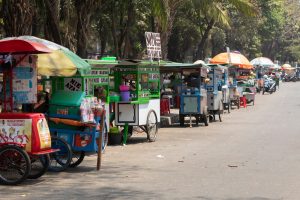 Gerobak makanan jalanan Indonesia dengan berbagai hidangan khas dan suasana ramai.