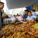 Penjual dan pembeli jajanan kaki lima di pasar kuliner, menawarkan aneka gorengan dan kue tradisional yang terbuka di atas meja