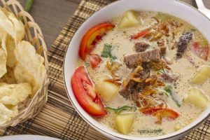 Soto Betawi khas Jakarta dengan kuah santan susu, potongan daging sapi, dan jeroan, disajikan dengan emping melinjo dan irisan daun bawang