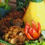 Tumpeng nasi kuning dengan hiasan sayuran segar, simbol kuliner tradisional Indonesia yang tetap relevan di era modern