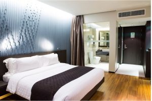 Interior kamar hotel modern dengan desain minimalis, tempat tidur king-size, pencahayaan hangat, dan suasana tenang yang cocok untuk relaksasi pekerja sibuk