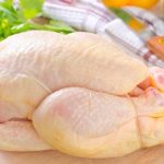 Fresh whole probiotic chicken on a wooden cutting board with vegetables in the background