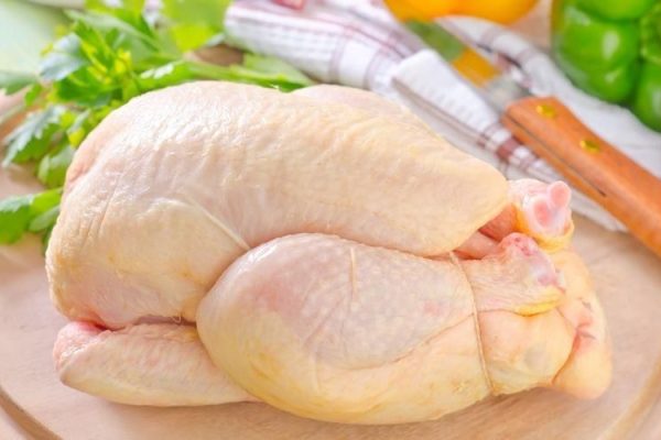 Fresh whole probiotic chicken on a wooden cutting board with vegetables in the background