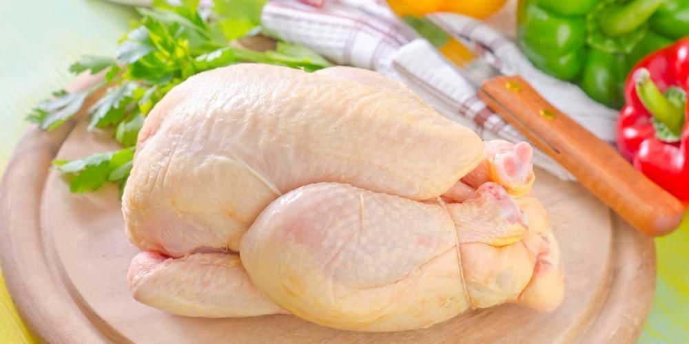 Fresh whole probiotic chicken on a wooden cutting board with vegetables in the background